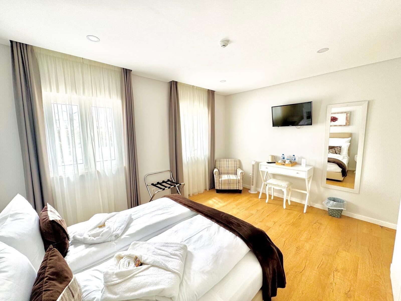 Una habitación de hotel con cama, escritorio, silla, televisor y espejo.