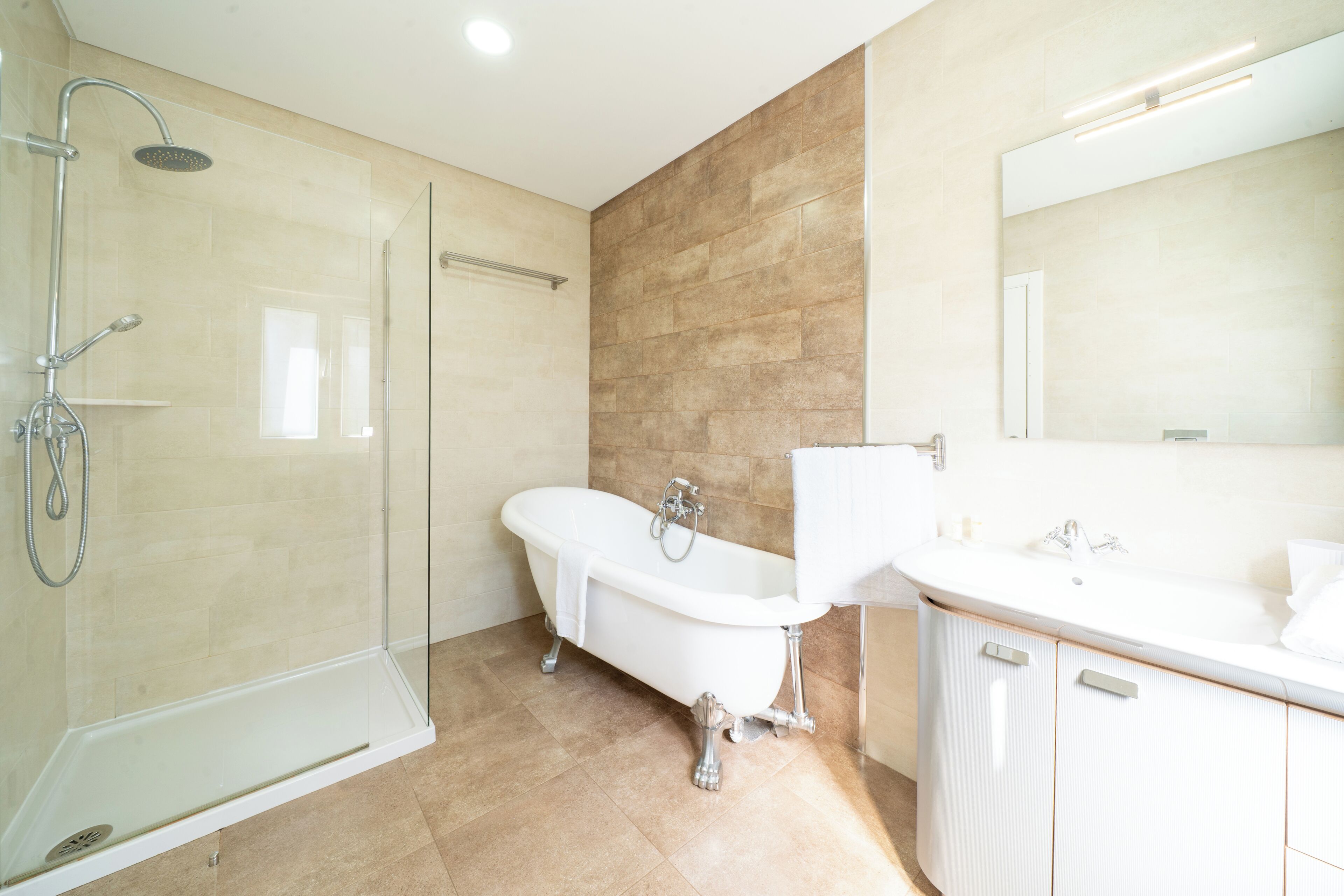 Een badkamer met een douche met glazen wand, een vrijstaand bad en een wastafel met spiegel.
