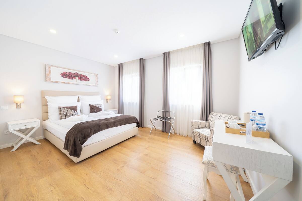 Een moderne hotelkamer met een bed, nachtkastje, stoel, bureau en een flatscreen televisie aan de muur.