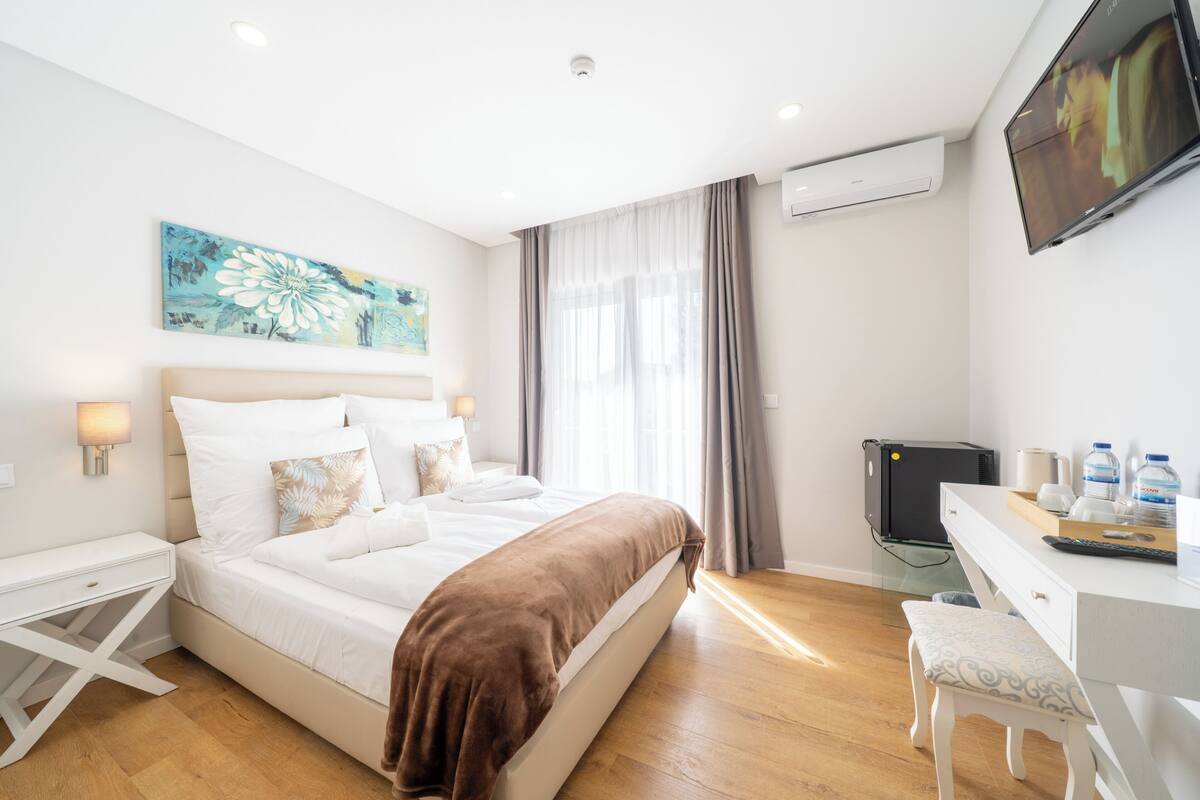 Een hotelkamer met een bed, nachtkastjes, een bureau met stoel, een televisie en een airconditioning.