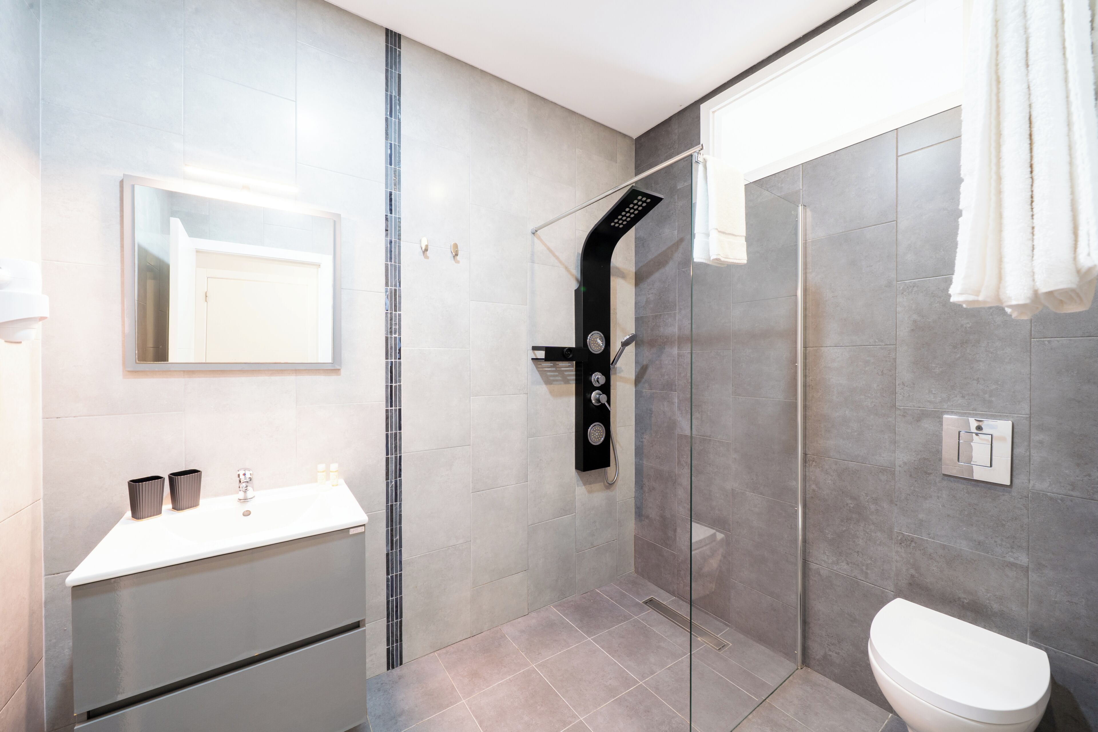 A modern bathroom with a glass-enclosed shower, a white toilet, and a vanity with a mirror.