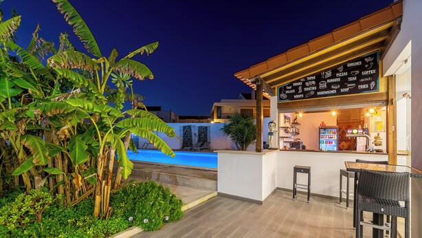 Un restaurante con zona de estar junto a la piscina, un cartel con la carta y una piscina al fondo.