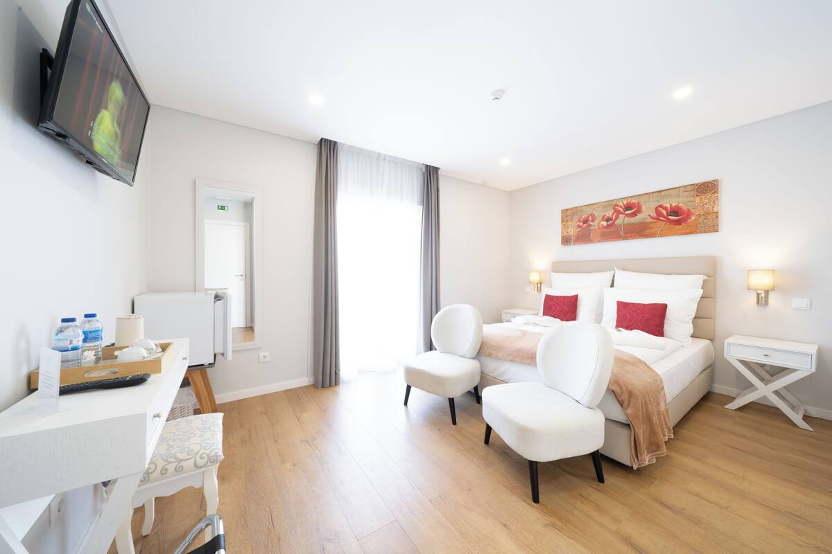 Een hotelkamer met een bed, twee stoelen, een bureau, een televisie en een schilderij aan de muur.