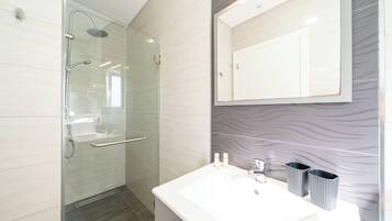 Une salle de bain moderne avec une douche à parois de verre, un lavabo blanc et un grand miroir.
