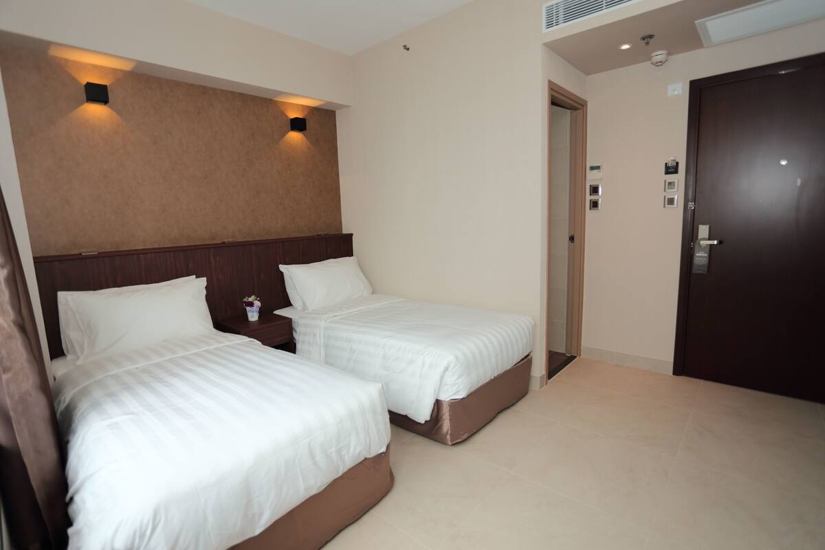 A hotel room with two beds, a wooden headboard, a small nightstand, and a door.