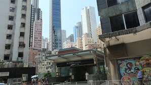 A cityscape with tall buildings, a covered entrance to a station, and a colorful mural on a wall. - WE Hotel (Hong Kong)