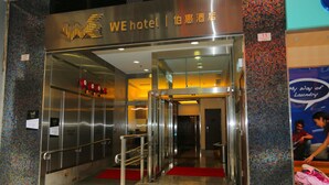 The entrance of a hotel with a modern design, featuring a metallic facade, a red carpet, and a digital display above the entrance. - WE Hotel (Hong Kong)