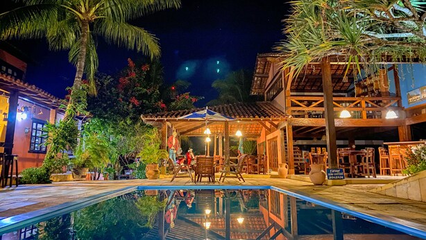 A nighttime pool area with a reflection of the building and palm trees. - Hotel Pousada Marambaia (Porto Seguro)