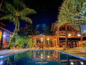 A nighttime pool area with a reflection of the building and palm trees. - Hotel Pousada Marambaia (Porto Seguro)