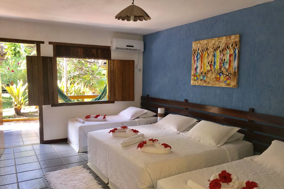 A hotel room with two beds, a large window, a painting on the wall, and a view of greenery outside.