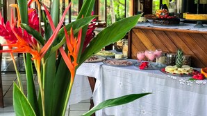 A table set with various food items and drinks, surrounded by tropical plants. - Hotel Pousada Marambaia (Porto Seguro)