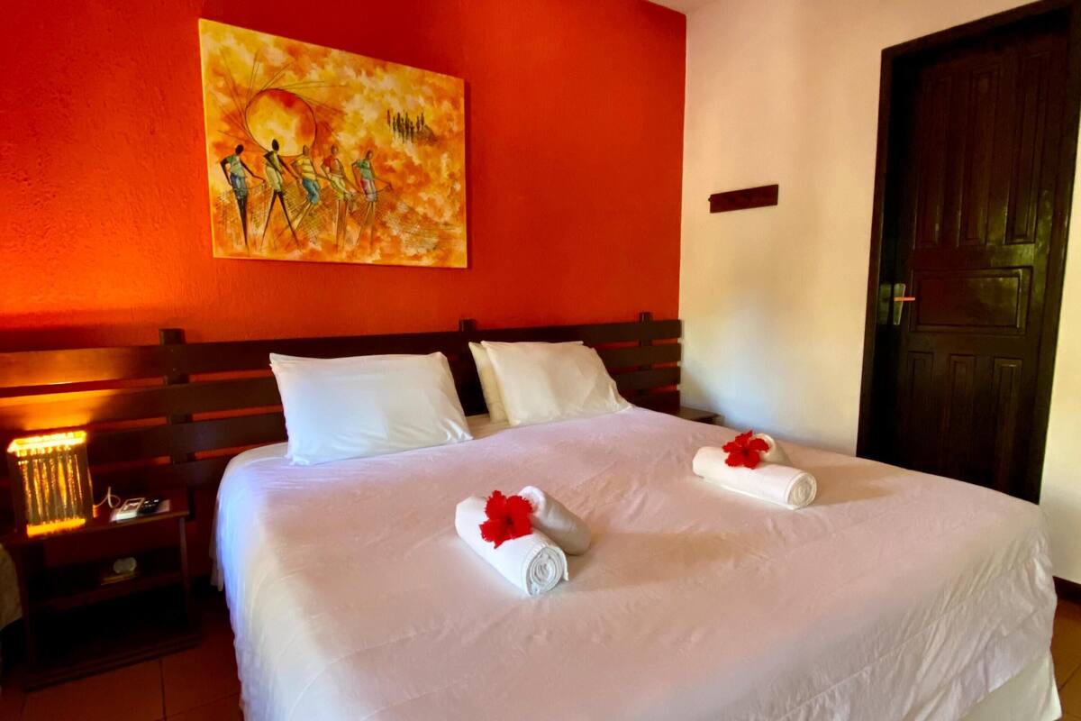 A hotel room with a large bed, white linens, and a painting on the wall.