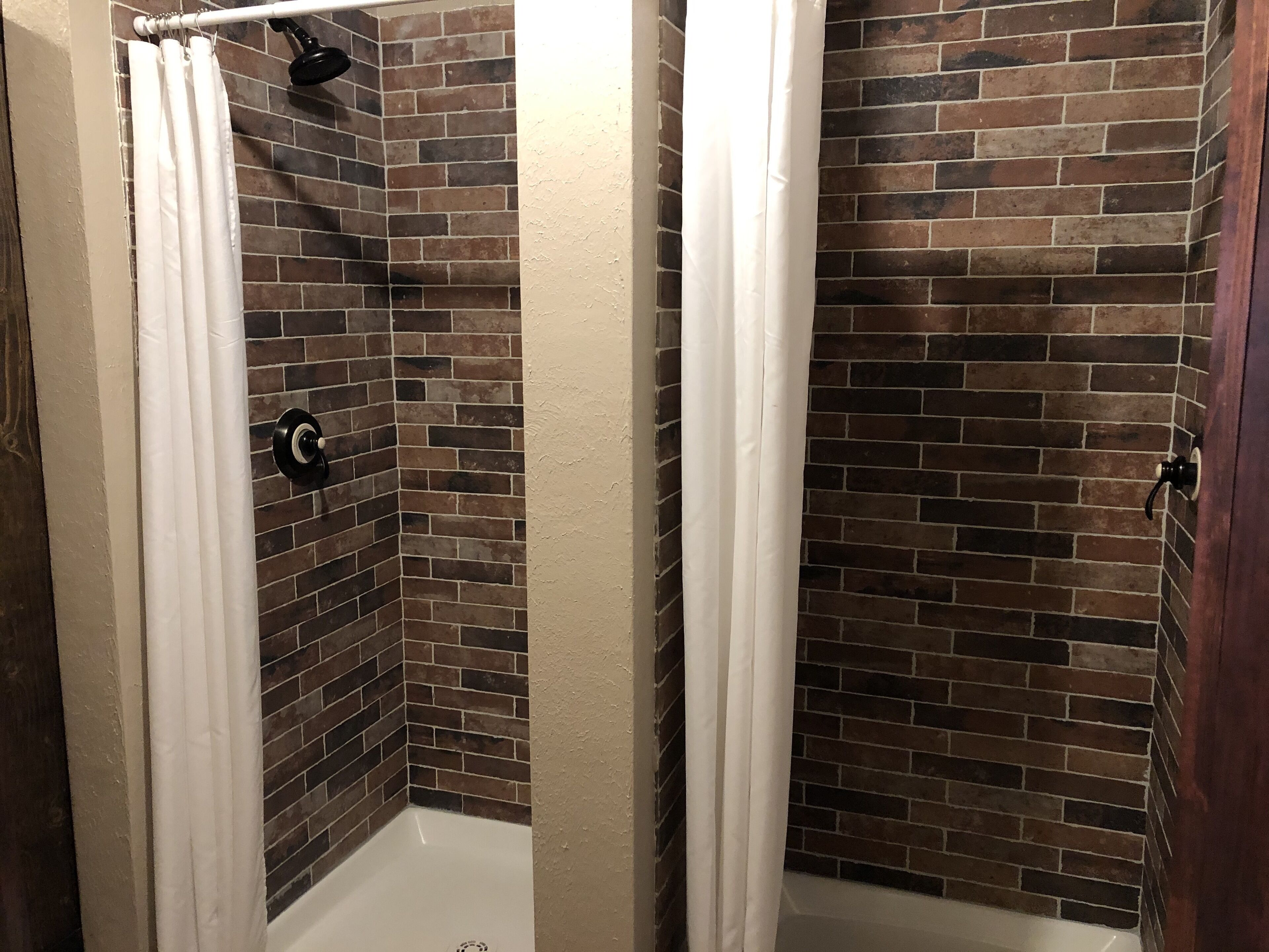 A shower with a brick wall, white curtain, and a handheld showerhead.
