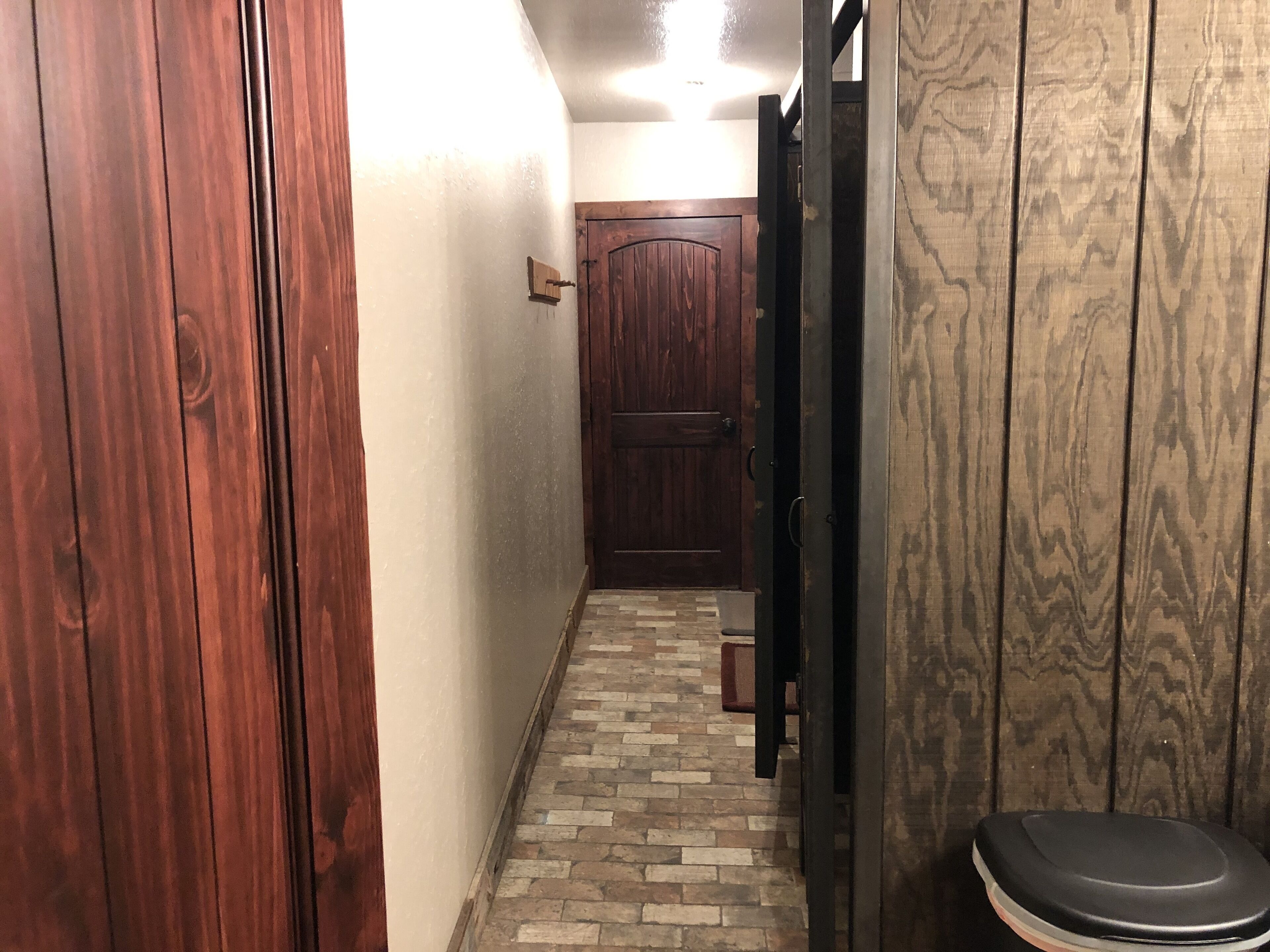 Un pasillo estrecho con una puerta de madera a la izquierda, una pared de madera a la derecha y suelo de baldosas.