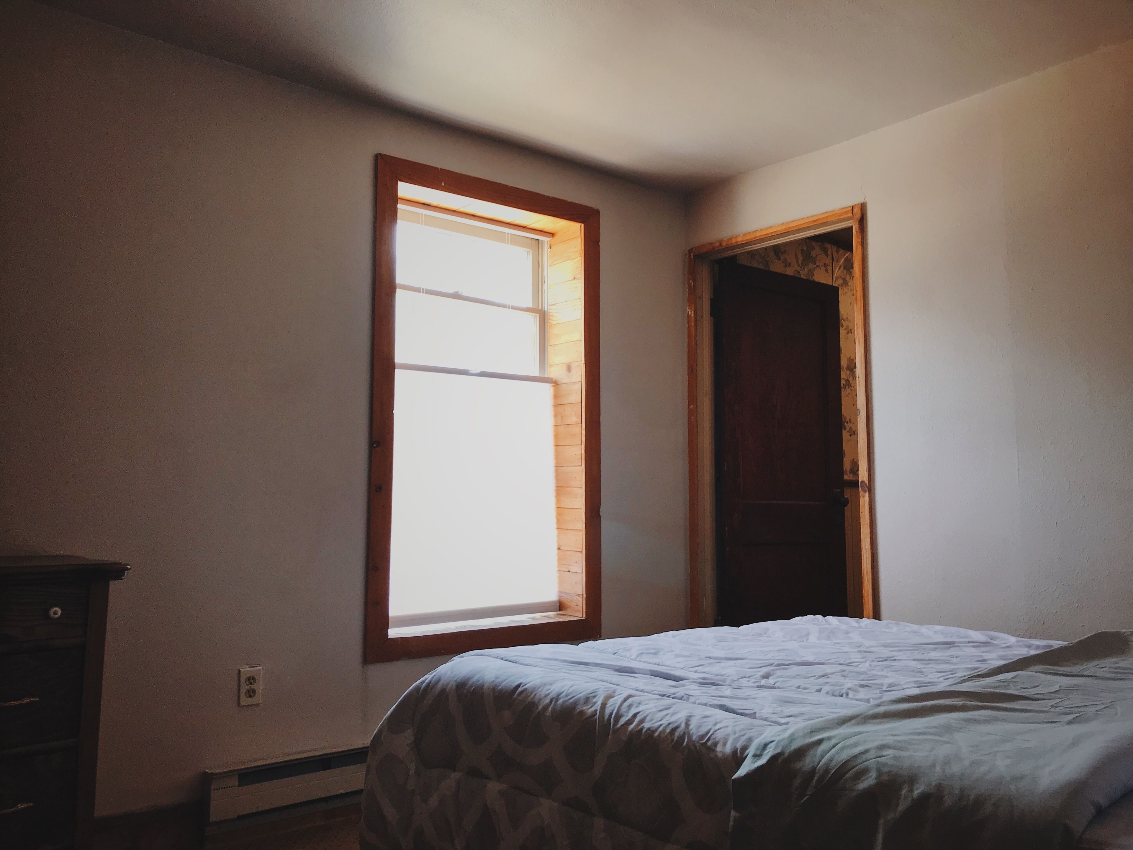 A bedroom with a bed, a window, and a door.