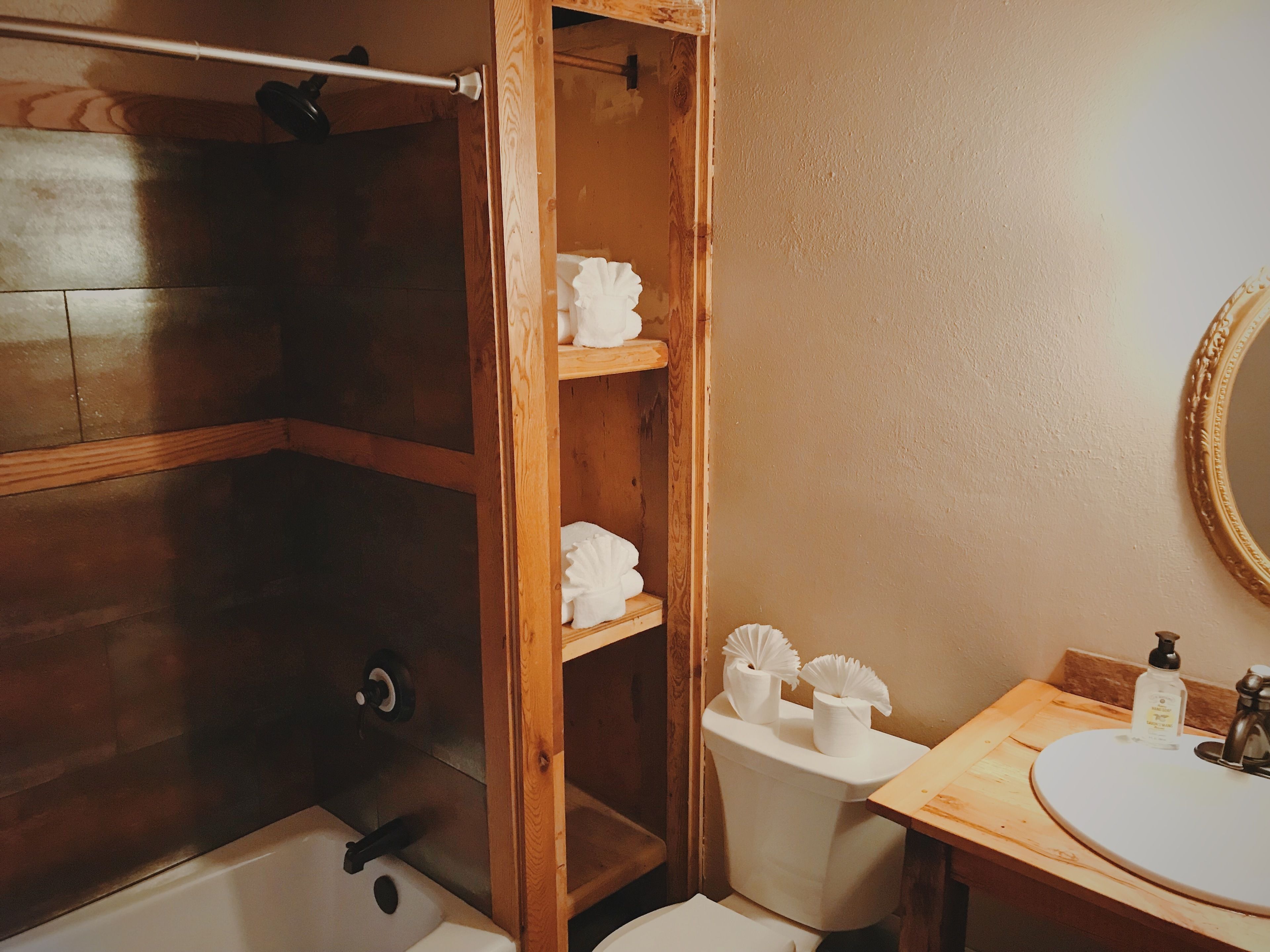 Een badkamer met een douchecabine van hout, een toilet en een wastafel met spiegel.