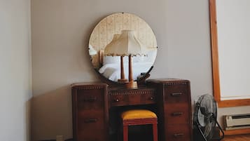 Un aparador de madera con espejo y un taburete en una habitación con piso de madera y un tapete estampado.