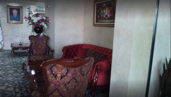 Una habitación con un sofá rojo, un sillón estampado, una mesita de madera, un jarrón con flores y un retrato enmarcado en la pared.
