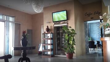A lobby with a television, a coffee shop sign, a bookshelf, and a potted plant.