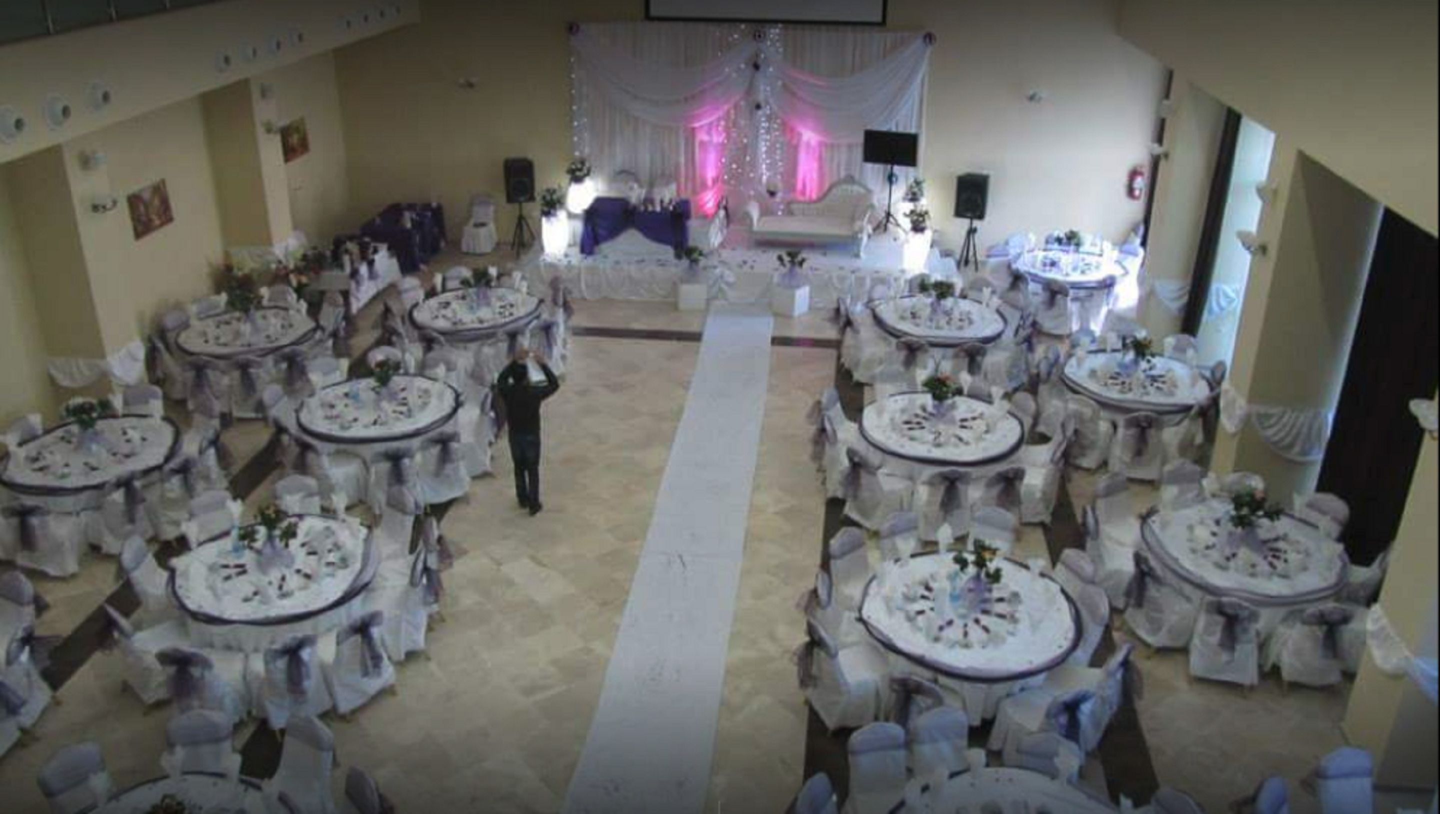 Un salón de banquetes con mesas redondas dispuestas en filas, un pasillo central y un escenario con cortinas.