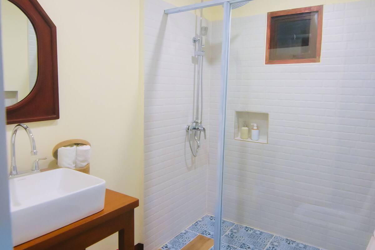 Une salle de bain équipée d’un lavabo, d’un miroir, d’un porte-serviettes, d’une douche et de toilettes.