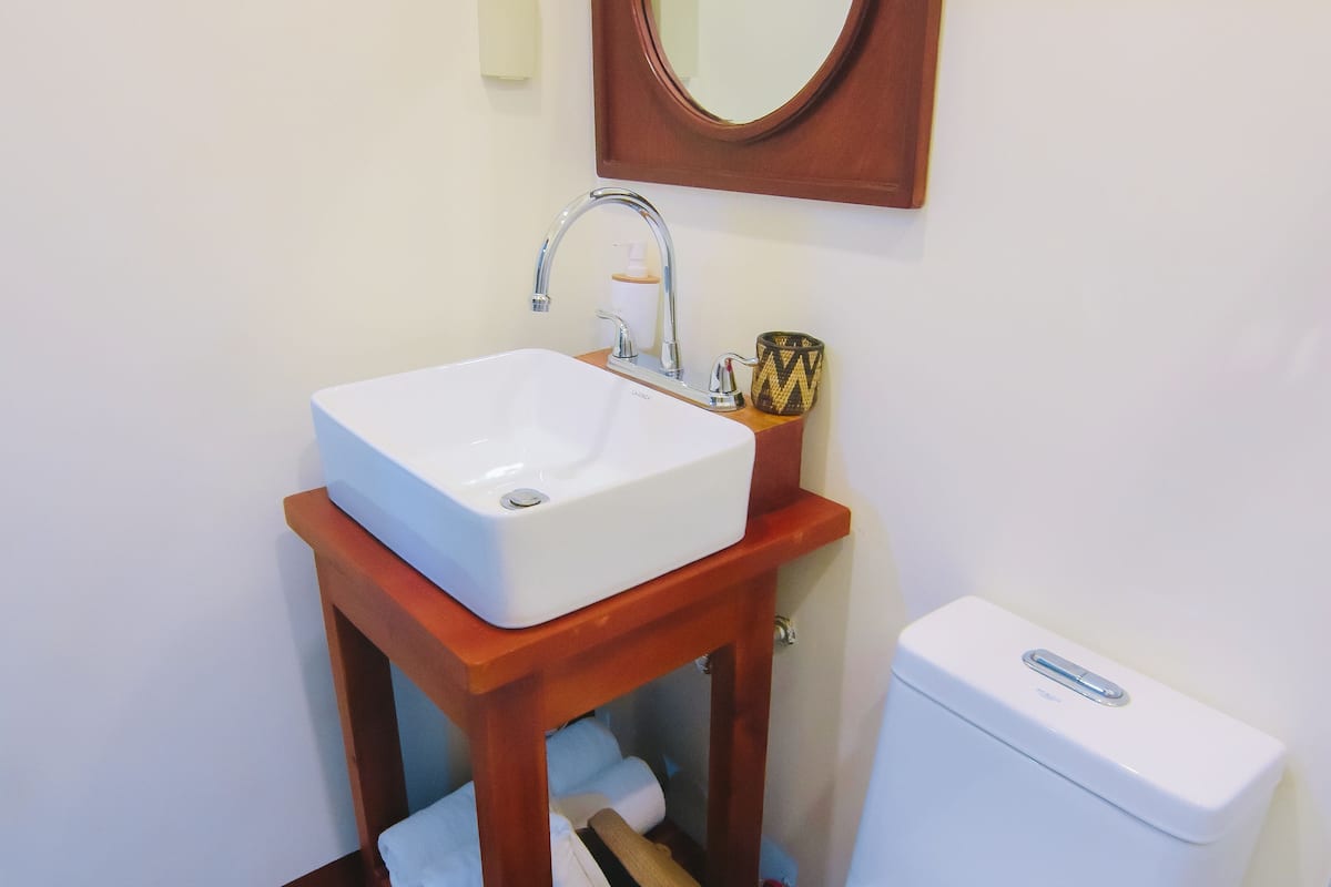 Une salle de bain avec un lavabo blanc, un meuble-lavabo en bois, un miroir, des toilettes et un tapis à rayures.