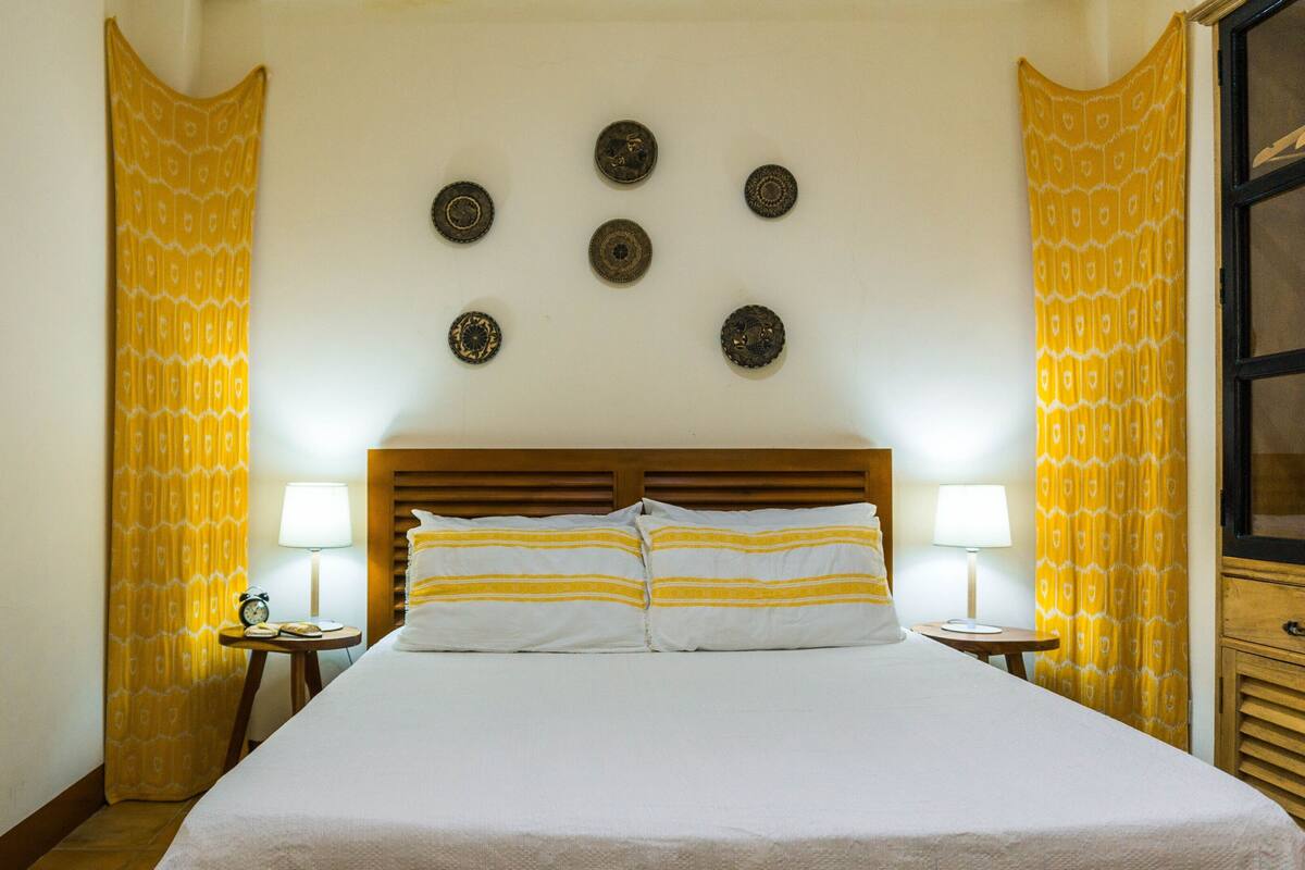 Une chambre d’hôtel comprenant un lit, deux tables de chevet, une horloge murale et des assiettes décoratives.
