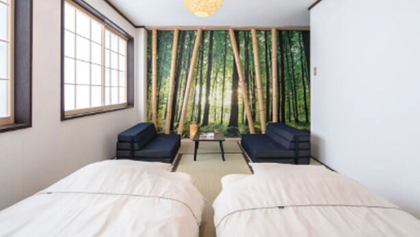 A room with two beds, a table, and chairs, with a bamboo forest mural on the wall. - Sakura Inn (Kyoto)