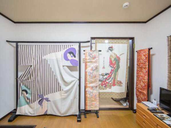 Une pièce dotée d’un paravent coulissant de style shoji, une porte coulissante traditionnelle japonaise, et d’un téléviseur posé sur une commode en bois.