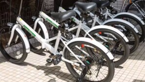 A row of white bicycles with black seats and handlebars, parked in an indoor area with a tiled floor. - Sakura Inn (Kyoto)