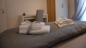 A neatly made bed with folded towels and a flat-screen TV mounted on the wall. - B&B da Francesco (Capaccio-Paestum)