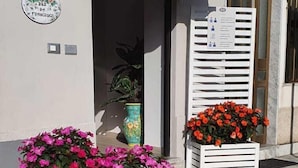 A building with a grey awning labeled 'B&B' and two white wooden planters with pink flowers. - B&B da Francesco (Capaccio-Paestum)