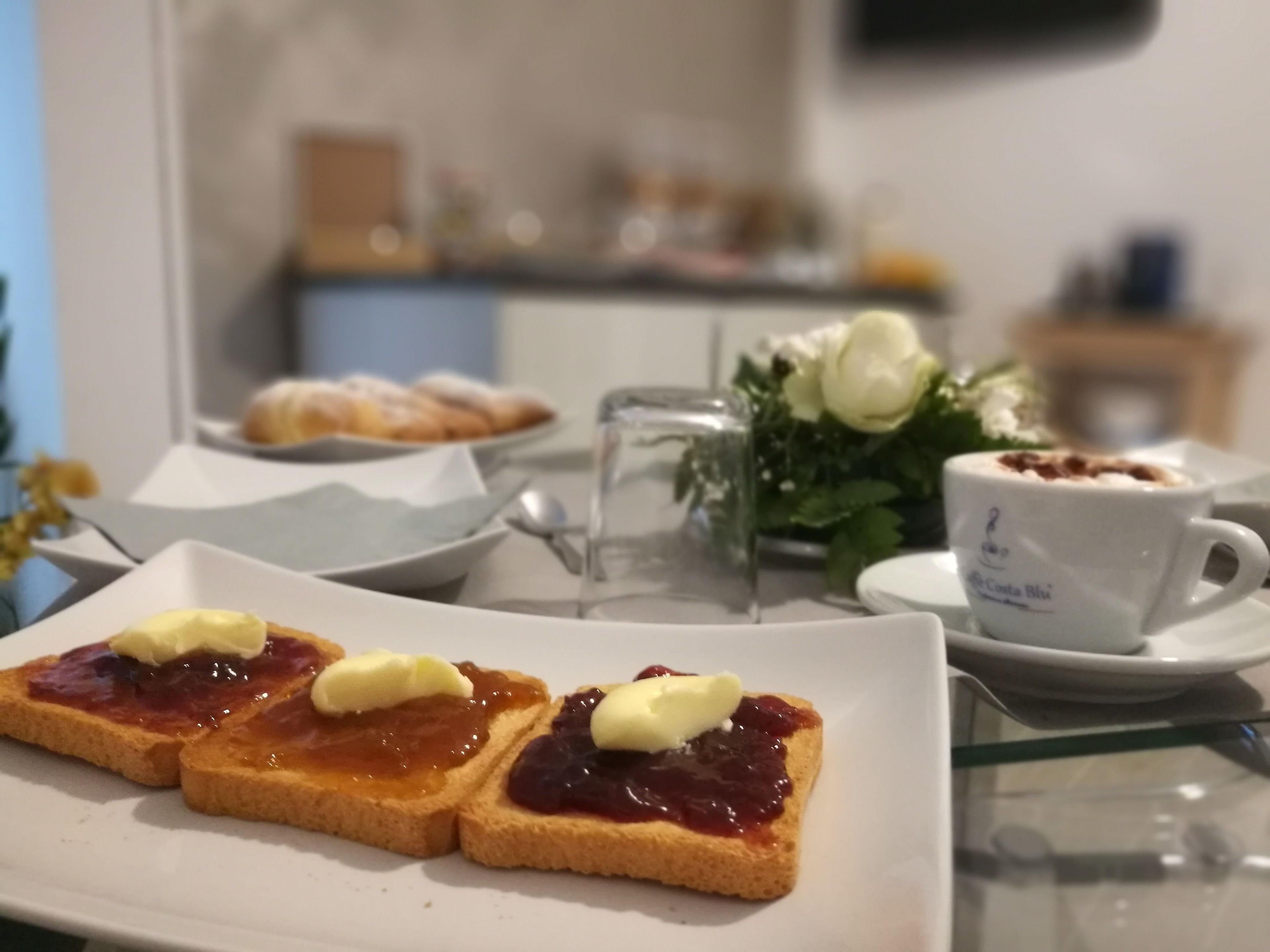 Esmorzar amb torrades, melmelada i mantega damunt d'un plat, una tassa de cafè i un ram de flors en un vas.