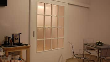 A room with a white door, a small table with a coffee machine, and a glass table with chairs.