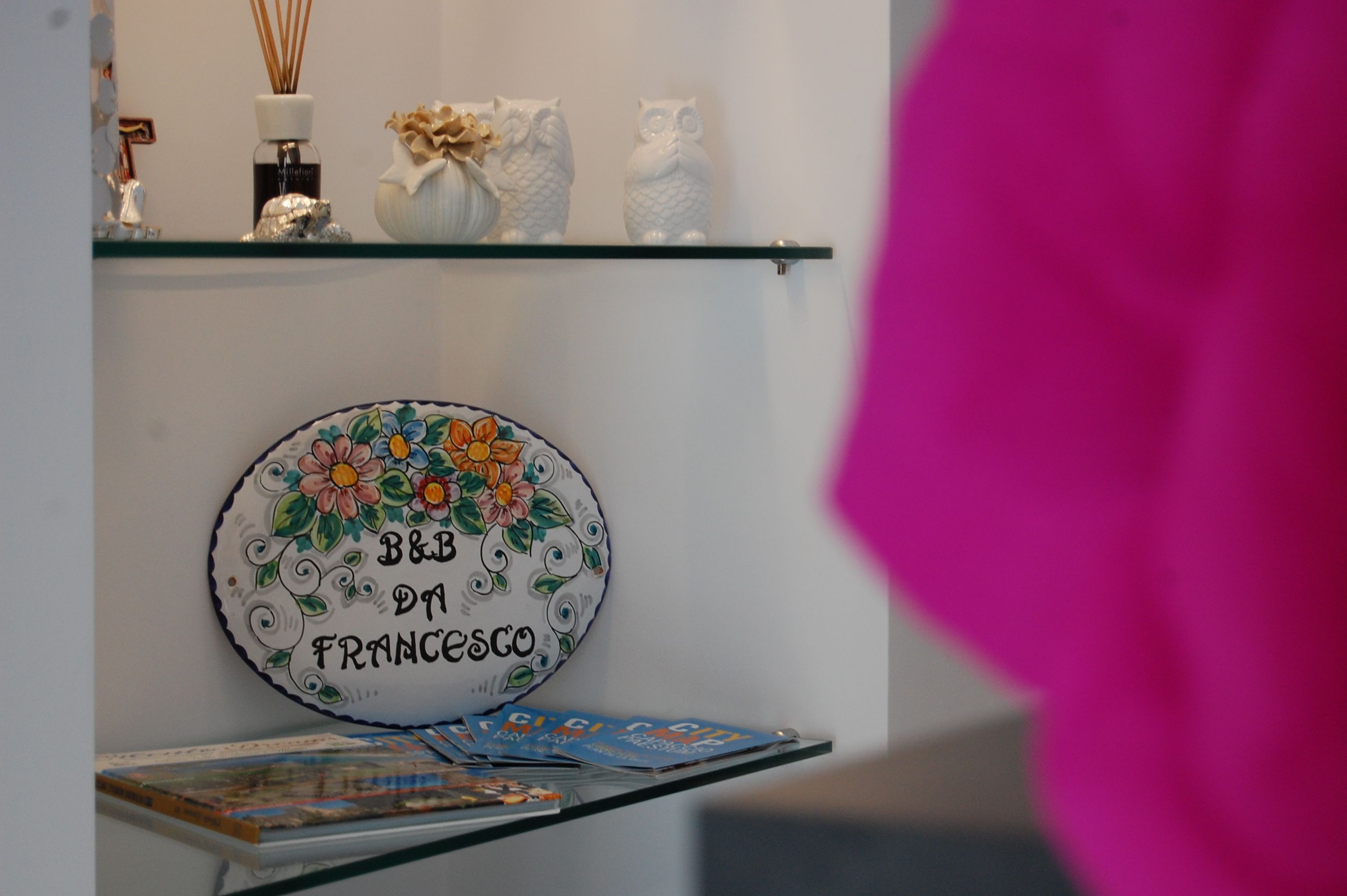 Un plato decorativo con diseños florales y texto, un estante de vidrio con varios objetos, y una revista sobre una mesa.