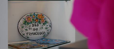 Un plato decorativo con diseños florales y texto, un estante de vidrio con varios objetos, y una revista sobre una mesa.
