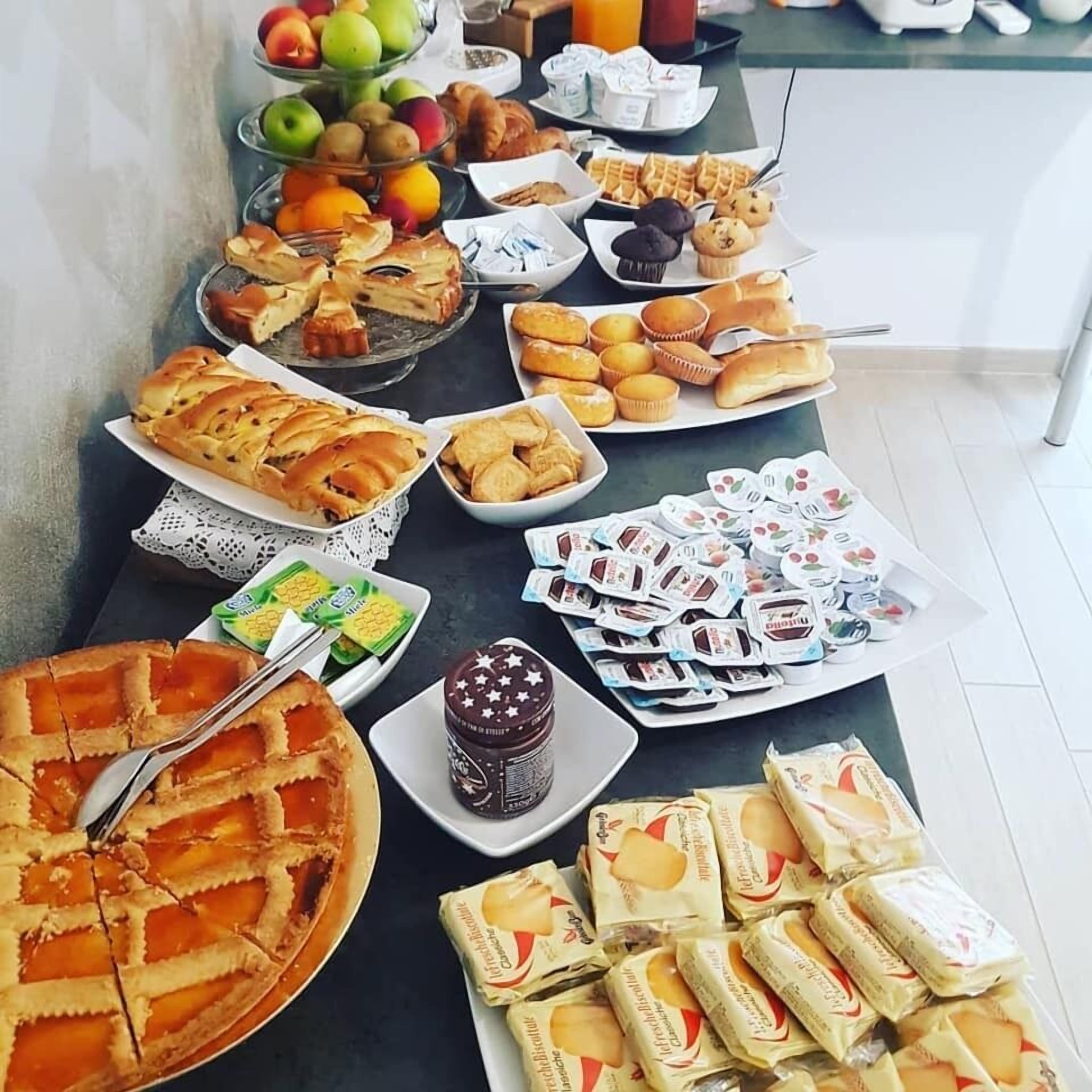 Una mesa de bufé con diversos alimentos, incluyendo pasteles, frutas y bocadillos envasados.