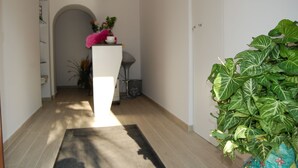 A hallway with a white reception desk, a large green plant, and a black rug. - B&B da Francesco (Capaccio-Paestum)