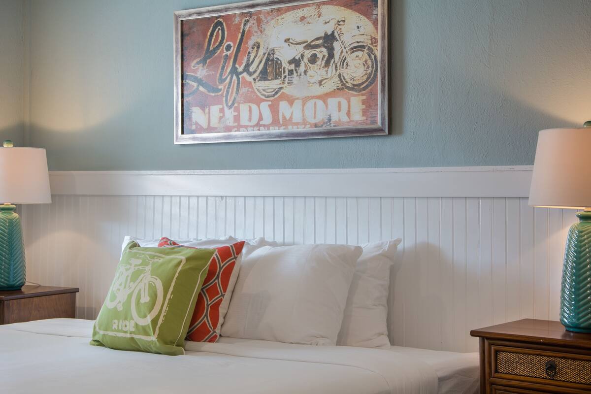 A hotel room with a bed, pillows, a wall-mounted sign, and two bedside lamps.