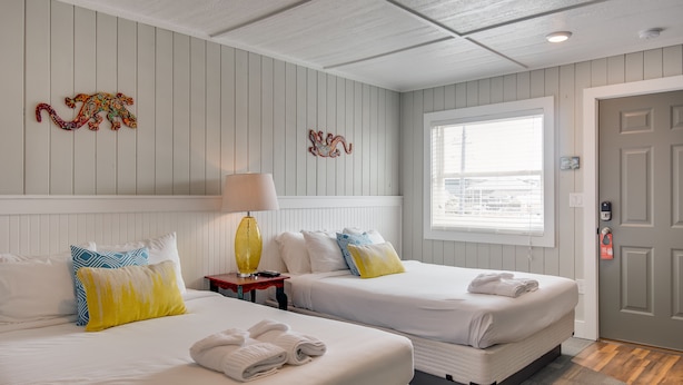 Habitación de hotel con dos camas, una ventana con persianas, una puerta con cerradura y un adorno en la pared.