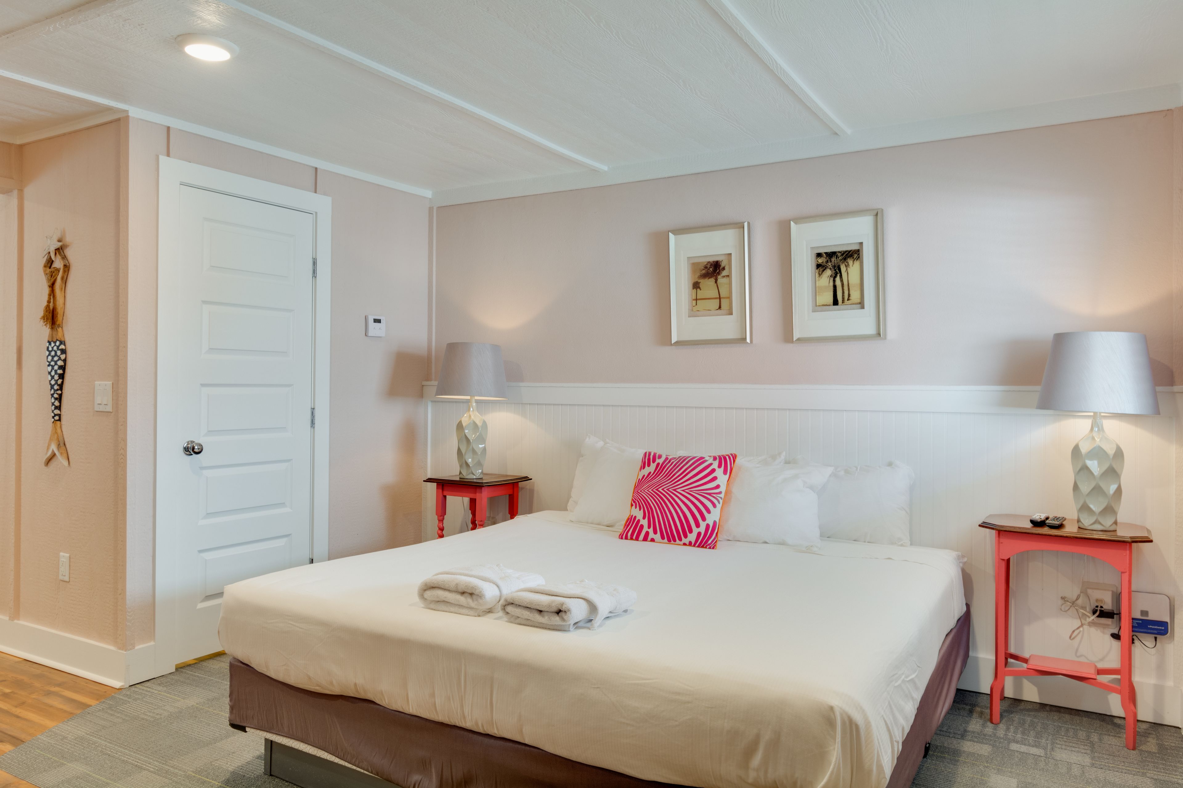 Een netjes ingerichte hotelkamer met een groot bed, twee nachtkastjes, een deur en twee ingelijste foto’s aan de muur.