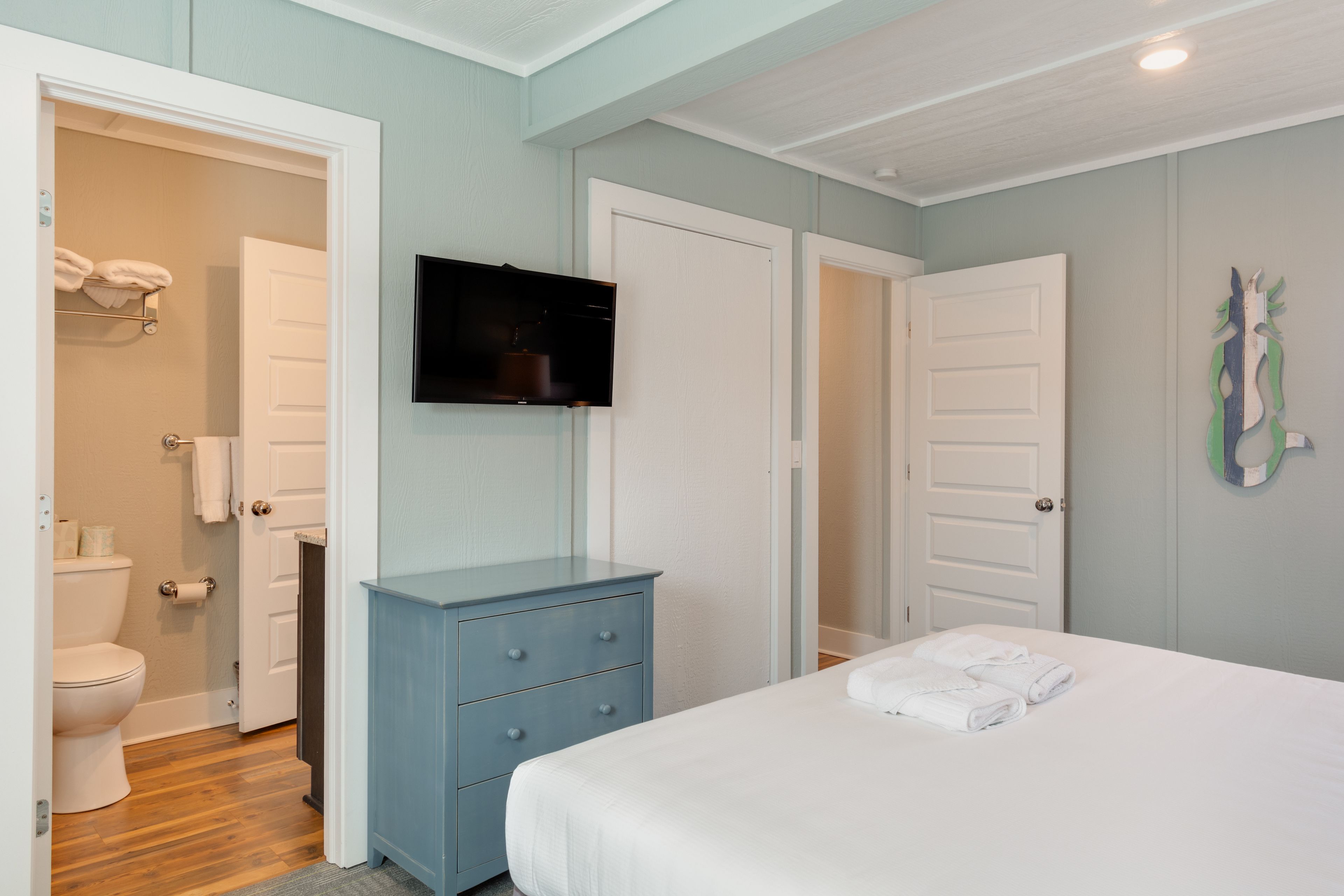 Un dormitorio con cama, cómoda, televisión y baño visible a través de una puerta abierta.
