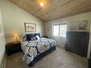 A bedroom with a bed, a nightstand, a lamp, a window, and a fireplace.