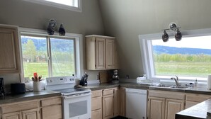 Une cuisine dotée de meubles en bois, d’une cuisinière, d’un lave-vaisselle et d’une grande fenêtre donnant sur un paysage verdoyant.