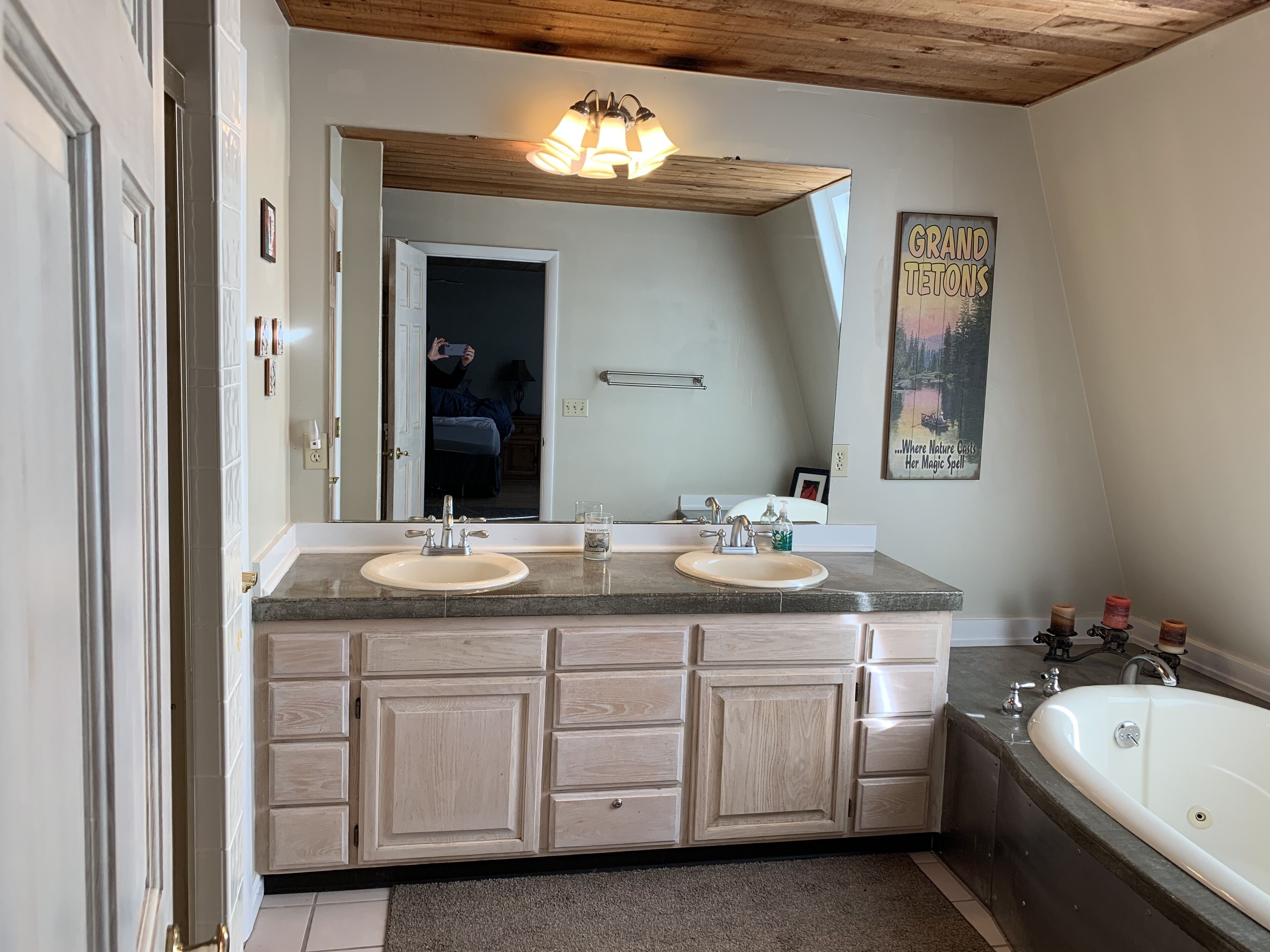 Ein Badezimmer mit zwei Waschbecken, einem großen Spiegel, Holzschränken, einer Badewanne und einer Deckenleuchte.