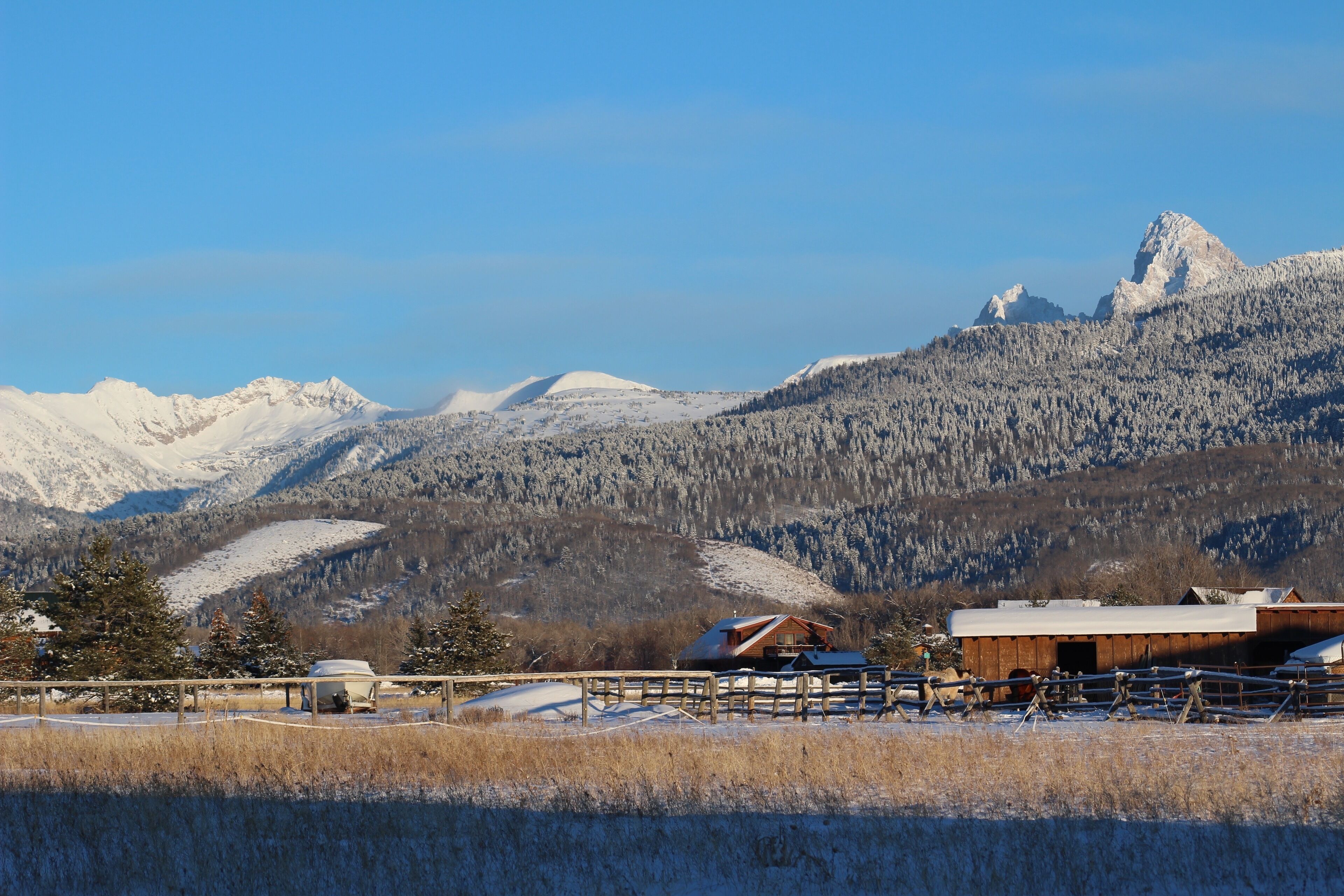 A mountain landscape with snow-covered peaks and a wooden cabin with a metal roof.