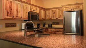 A kitchen with wooden cabinets, a stainless steel refrigerator, a microwave, an oven, and a granite countertop.