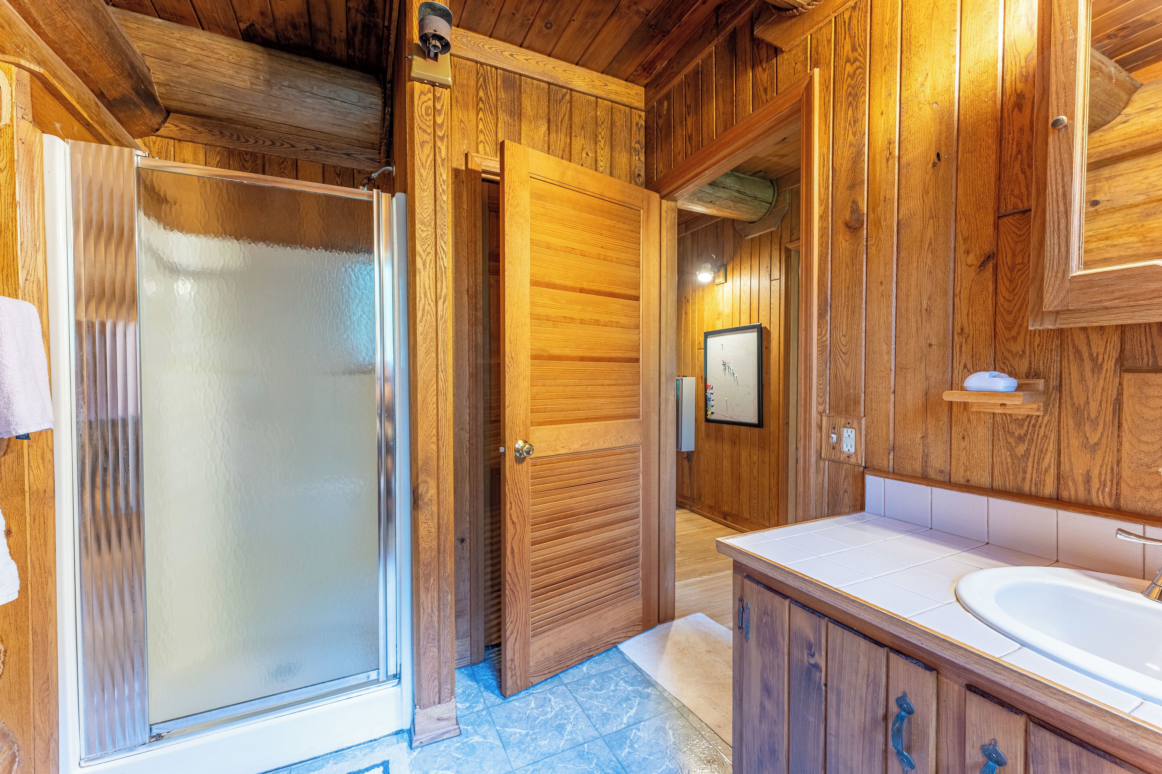 Een houten badkamer met een glazen douchedeur, een houten wastafel en een wasbak.