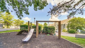 Ein Spielplatz mit Rutsche und Schaukeln, umgeben von Bäumen und Wohnhäusern.