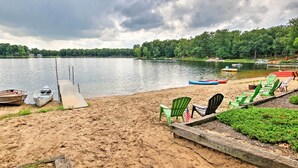 Ein See mit Strand, einer Holzsteg und Liegestühlen in Grün und Schwarz, sowie eine Reihe von Booten.